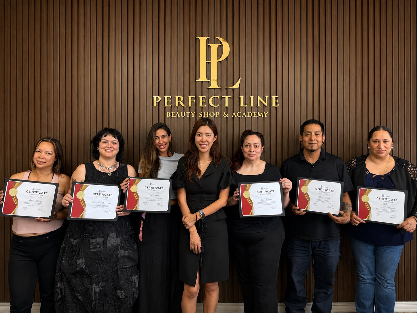 Graduating cohort holding Certificates of Completion with Master Artist Yu-Jin Lee at the Perfect Line Academy logo wall