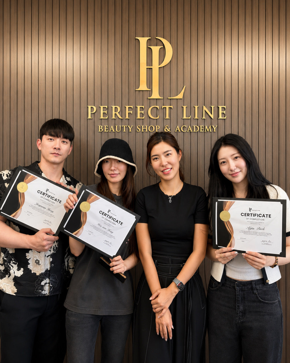 Four graduates holding Certificates of Completion with Master Artist Yu-Jin Lee at the Perfect Line Academy logo wall